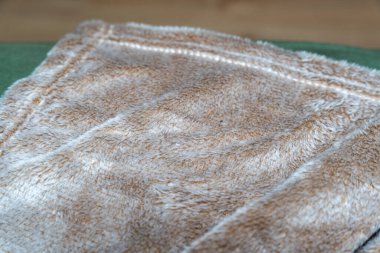 Yumuşak ve rahat bej battaniye yeşil bir kanepede düzgünce katlanmış. Bu sıcak tekstil herhangi bir yaşam alanına rahatlık katar ve basit bir dokunuşla ev dekorunu geliştirir..