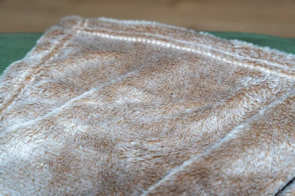 Yumuşak ve rahat bej battaniye yeşil bir kanepede düzgünce katlanmış. Bu sıcak tekstil herhangi bir yaşam alanına rahatlık katar ve basit bir dokunuşla ev dekorunu geliştirir..