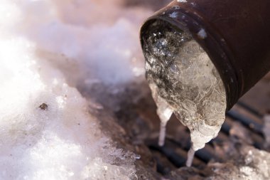 Soğuk bir yüzeyde eriyen karla çevrili kahverengi bir metal kutudan eriyen buzun yakın çekim görüntüsü. Sahne, kış ve bahar arasındaki geçişi kaydediyor. Açık buz oluşumlarını gösteriyor..