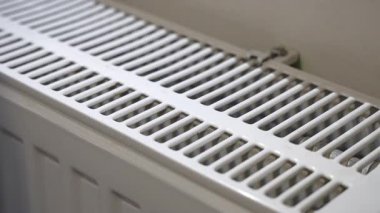 Soğuk kış boyunca içeride ısınmak için radyatörün üstünde el ele tutuşan bir adam.