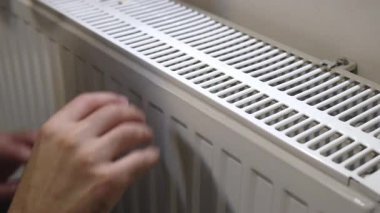 Evdeki soğuk kış gününde iki elini de radyatörde ısıtan adam.