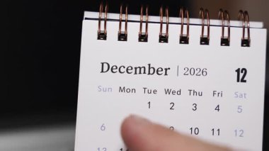 Bir dizüstü bilgisayar klavyesine insan parmağı olarak yerleştirilen bir masa takviminin yakın çekimi Aralık 2026 'daki belirli bir tarihi gösteriyor. Kamera sabit duruyor, net tarih seçimi ve yıl sonu planlama kavramını kapalı tutuyor.