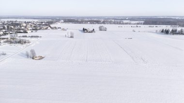 Uçsuz bucaksız karla kaplı bir arazinin arka planda uzak yerleşim evleri mevsimsel promosyon ve reklamlar için ideal sakin bir kış manzarası oluşturuyor..