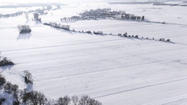 Beyaz ağaçlar ve tarlalarla kaplı kırsal bir alana sahip karla kaplı bir arazinin havadan görünüşü. Parlak bir kış gününde doğanın sakinliğini gösterirken yakalandılar..