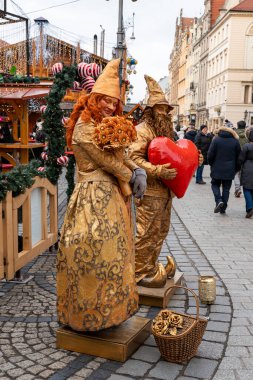Wroclaw Polonya - 3 Ocak 2026: Elfler gibi giyinmiş renkli sokak sanatçıları Wroclaw 'daki bir tatil pazarında kalabalıkları eğlendirip ziyaretçiler için şenlikli bir ortam yarattılar.