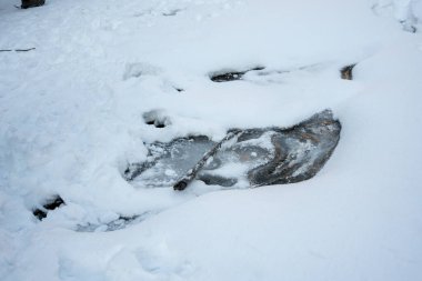 Kış manzarasında kısmen karla kaplı donmuş bir yüzey. Bu sahnede pürüzsüz bir buz tabakası ve doğada soğuk ve sakin bir atmosferi çağrıştıran bir sopa var..