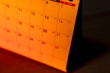 Ayın sıcak turuncu ışıltılı tarihlerini gösteren takvimin yakın plan görüntüsü. Zaman yönetimi planlaması ve organizasyonu kavramlarını resmetmek için ideal.