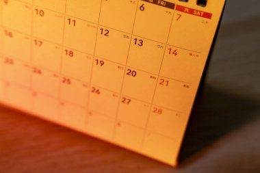 Bir takvim sayfasının yakın plan görüntüsü sıcak bir ışık ile gösterilen tarihler net bir düzende rakamları ve karakterleri gösteriyor. Zaman yönetimi temaları için ideal.