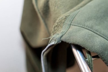 Görünür dikişli yeşil bir sweatshirt 'ün yakın çekimi ve fermuar detayı kumaş dokusunu gösteriyor. Tekstil endüstrisi için ideal moda pazarlama veya giyim tasarımı.