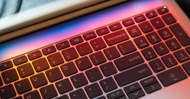 BACKSPACE ve ENTER tuşlarını gösteren ışıklı tuşlara sahip bir dizüstü bilgisayarın yakın görüntüsü. Renkli ışık efektleri modern ve teknolojik bir atmosfer yaratıyor..