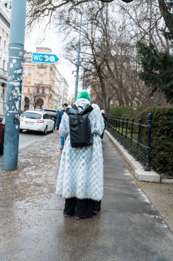 Vienna Austria- Feb 21 2026: A person walking down a city sidewalk in a stylish long coat adding a vibrant touch to a cold winter day surrounded by urban architecture.