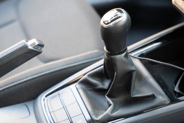 Modern bir aracın içinde bulunan vites kolu ve el freninin yakın görüntüsü deri detayları ve parlak tasarımı vurguluyor..