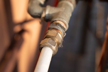 Endüstriyel ortamda beyaz bir boruyu metal bir vanaya bağlayan pirinçten yapılmış yakın çekim. Tesisat uygulamalarında ustalık ve kullanım gücü gösteriliyor..