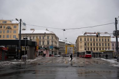 Viyana - 21 Şubat 2026: Arka planda tarihi binalar ve yolda bir toplu taşıma otobüsü bulunan caddeden geçen yayaları yakalayan karlı bir şehir manzarası.