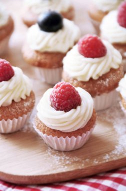 Krem peynir ve böğürtlenli güzel, lezzetli kekler. Yabanmersini ve ahududu. Ahşap ve kırmızı arka plan. Şirin mini kekler. 