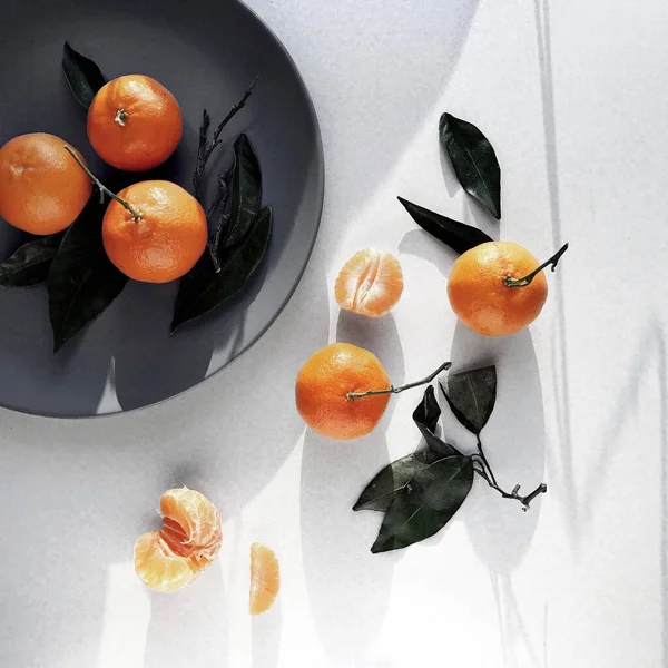 Clementines, beyaz masa, gri tabak, Noel atmosferi, sabah güneş ışığı, gölgeler, turuncu, minimalizm, üst görüş.