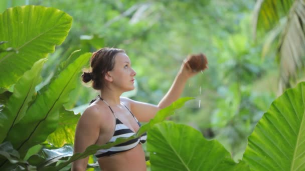 Женщина в бикини сидит в тропическом саду — стоковое видео