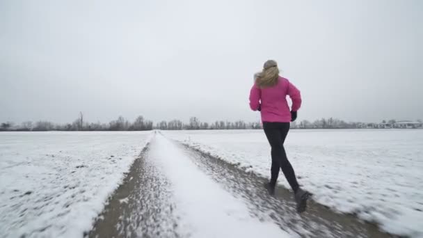 Жінка біжить по засніженій дорозі — стокове відео