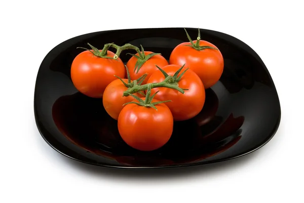 Tomates maduros en un plato negro sobre un fondo blanco — Foto de Stock