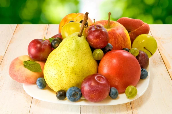 Different fruits on a plate on a green background — Stock Photo, Image