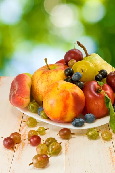 Different fruits on a plate on a green background — Stock Photo, Image