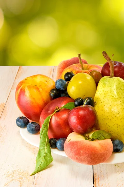 Different fruits on a plate on a green background — Stock Photo, Image