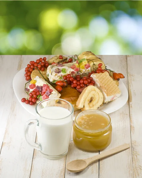 Imagen de platos con galletas, taza con leche y miel sobre la mesa sobre fondo verde —  Fotos de Stock