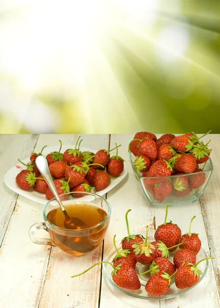 Φράουλες σε ένα πιάτο και ένα φλιτζάνι τσάι από τον ήλιο — Φωτογραφία Αρχείου