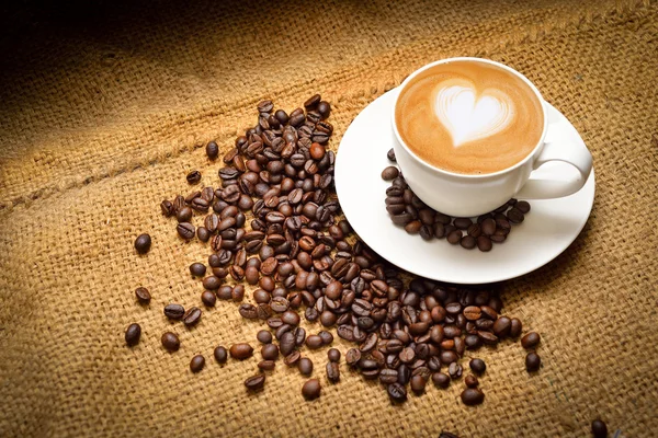 Secangkir kopi dengan latte seni hati dan kopi kacang pada latar belakang testure — Stok Foto