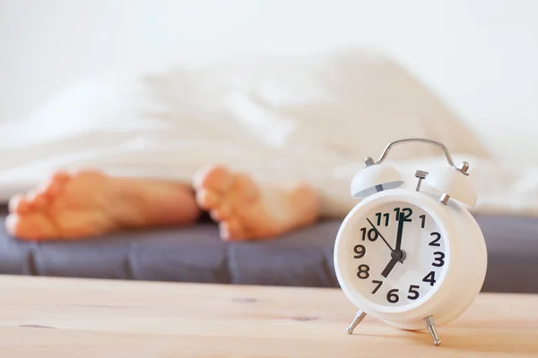 Alarm clock and feet of sleeping person — Stock Photo, Image