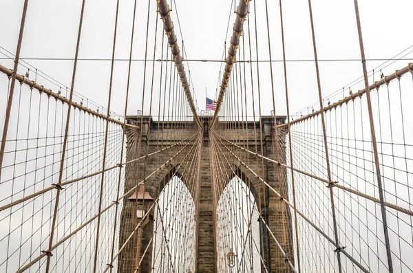 Low Angle View of Brooklyn Bridge Top with the American Flag Waving Proud in Manhattan, New York City, USA