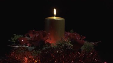 Ortasında parlak gümüş bir mum olan Noel çelengi ve etrafında altın süslemeler