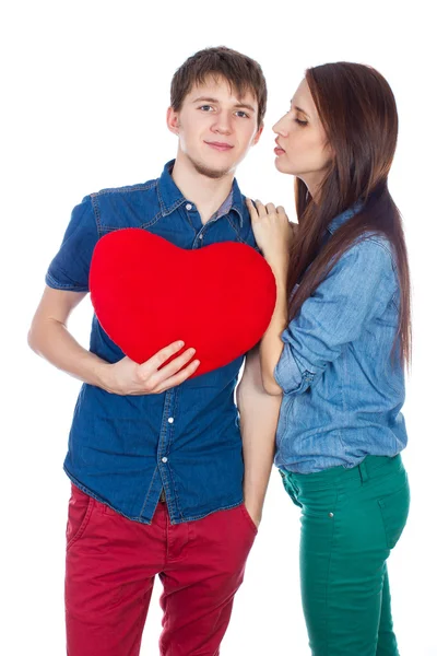 Eautiful young happy couple kissing behind a red heart, holding it in hands, isolated on a white background — Stock Photo, Image