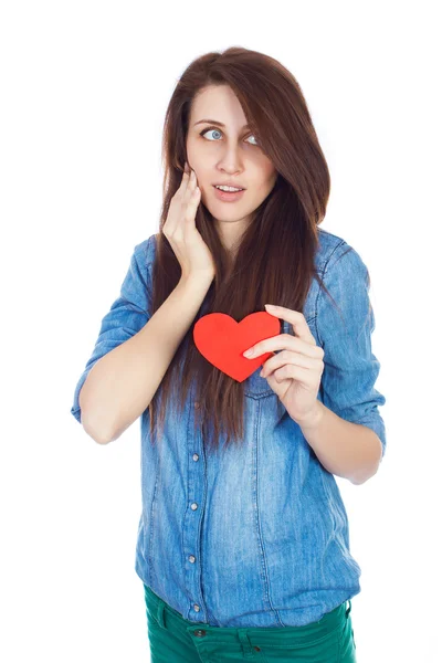 Bella ragazza in camicia blu denim in piedi su uno sfondo bianco con un cuore di carta rossa in mano . — Foto Stock