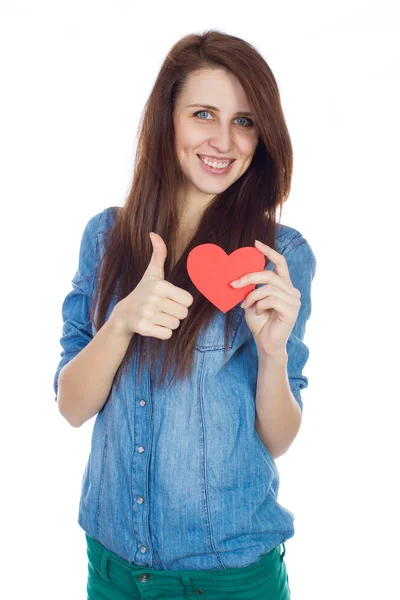 Bella ragazza in camicia blu denim in piedi su uno sfondo bianco con un cuore di carta rossa in mano . — Foto Stock