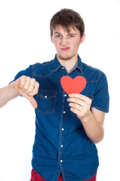 Beau jeune homme en denim chemise bleue debout sur un fond blanc avec un coeur en papier rouge dans les mains . — Photo