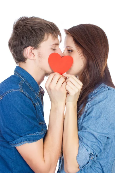 Beautiful young happy couple kissing behind a red heart, holding it in hands,  isolated on a white background — Stock Photo, Image