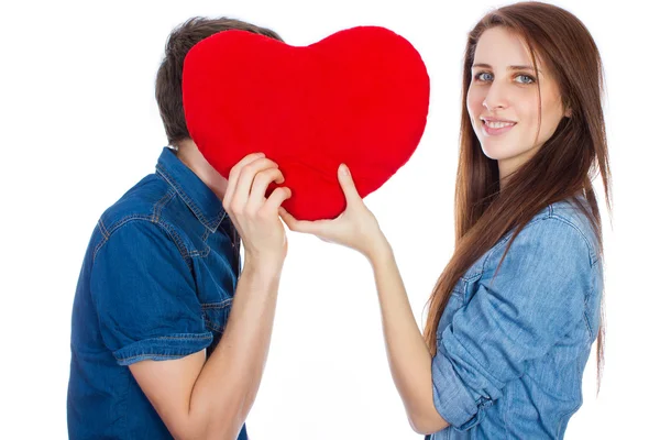 Beautiful young happy couple kissing behind a red heart, holding it in hands,  isolated on a white background — Stock Photo, Image