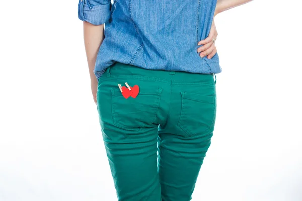 Uma mulher de camisa jeans azul e jeans verde em pé isolada em fundo branco com um coração de papel vermelho no bolso de trás — Fotografia de Stock