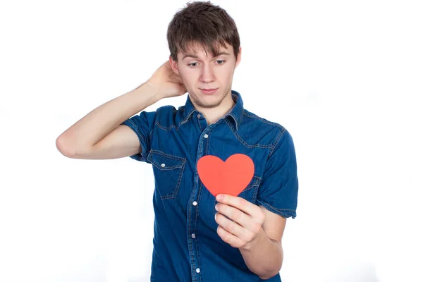 Knappe jongeman in denimblauw shirt staande op een witte achtergrond met een hart rode papier in handen. Rechtenvrije Stockfoto's