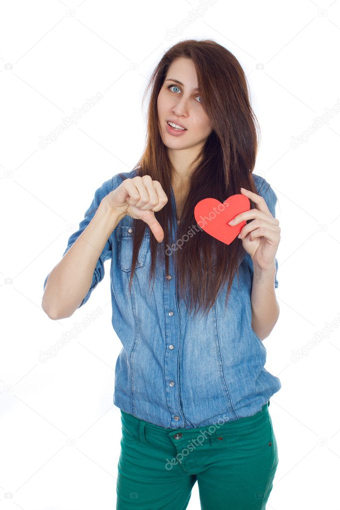 Beautiful young girl in denim blue shirt standing on a white background with a red paper heart in hands.