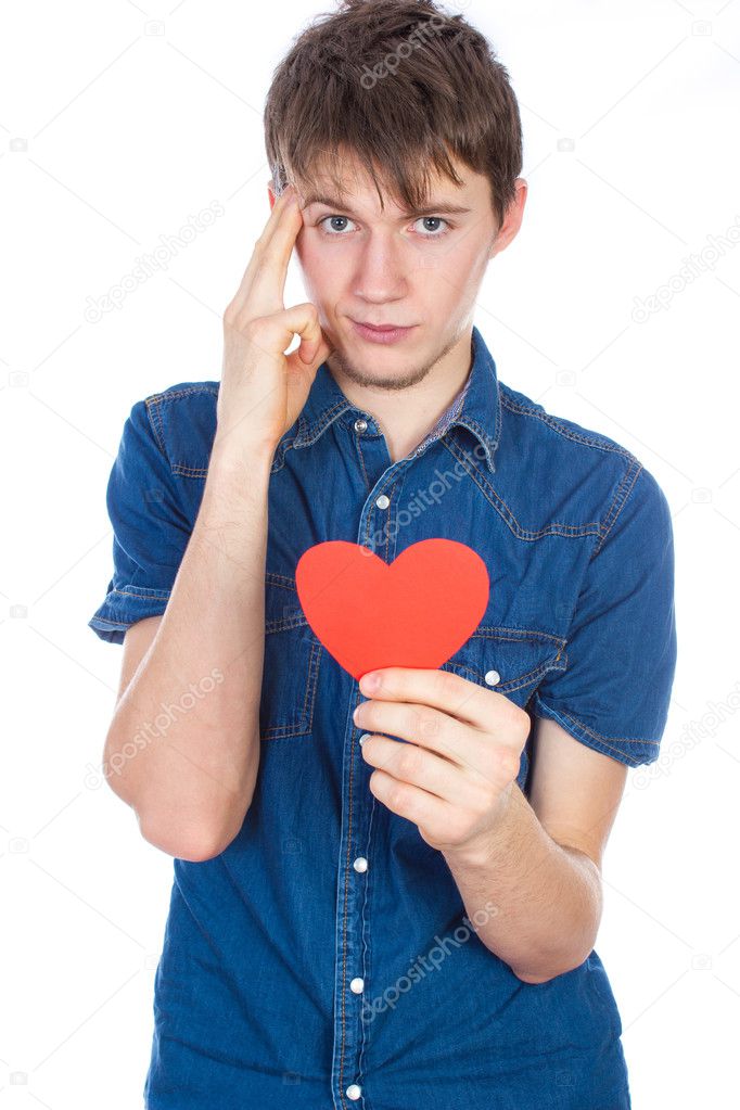 Handsome young man in denim blue shirt standing on a white background with a red paper heart in hands.