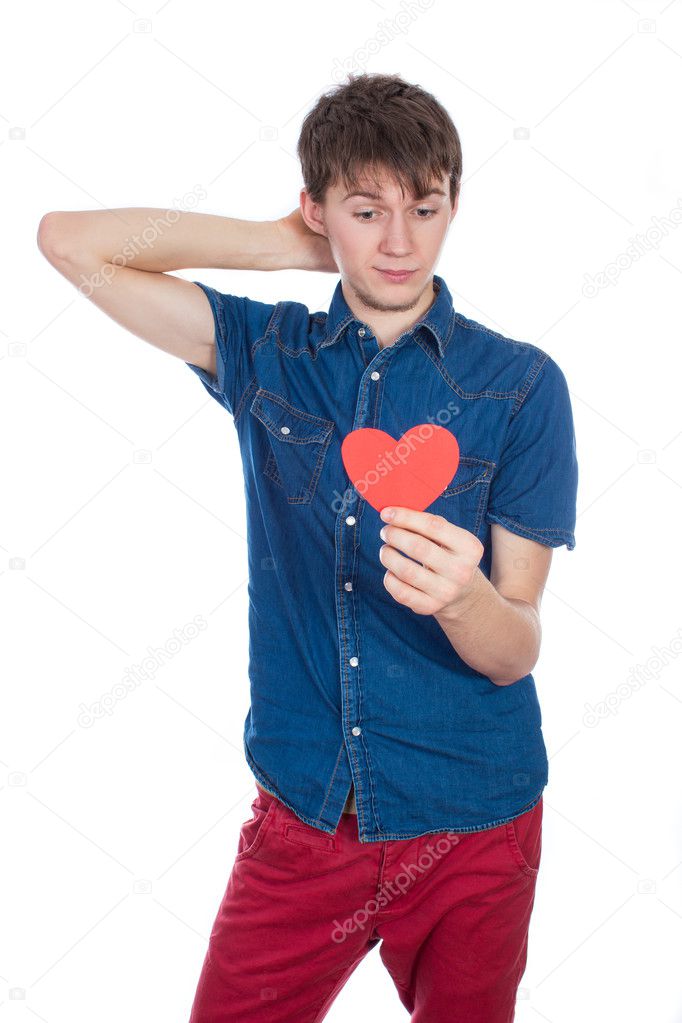 Handsome young man in denim blue shirt standing on a white background with a red paper heart in hands.