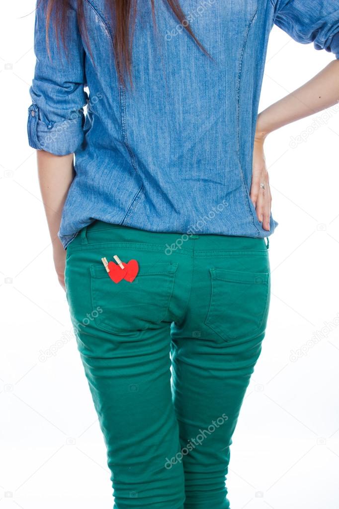 A woman in a blue denim shirt and green jeans standing isolated on white background with a red paper heart in your back pocket