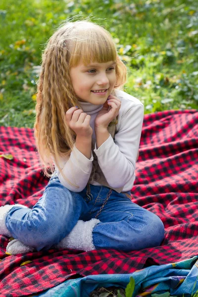 Bebé pequeno bonito sentado em uma planície vermelha. Criança encantadora sorrindo com flores brilhantes — Fotografia de Stock