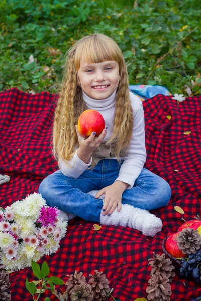 Beautiful little young baby in a pink hat with an apple in his hand. Beautiful child sitting on a red plaid. — Stock Photo, Image