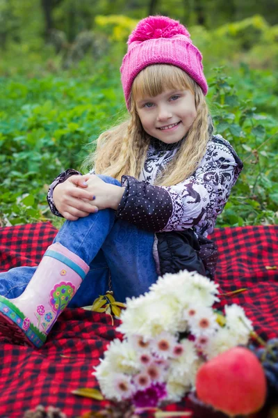Beautiful little young baby in a pink hat. Beautiful child sitting on a red plaid. — Stock Photo, Image