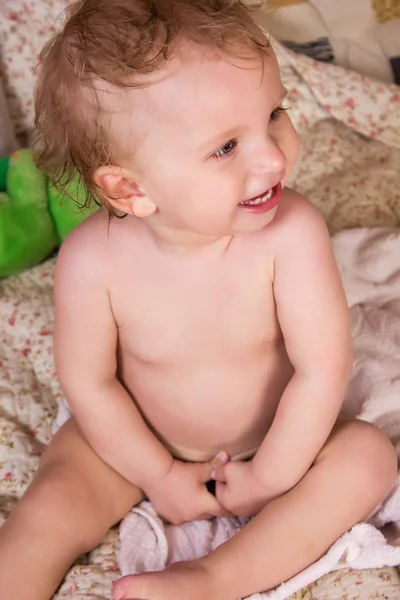 Roztomilá blonďatá holčička s krásné modré oči sedí na posteli a s úsměvem — Stock fotografie