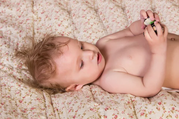 Linda niña rubia con hermosos ojos azules acostada en la cama con juguete —  Fotos de Stock