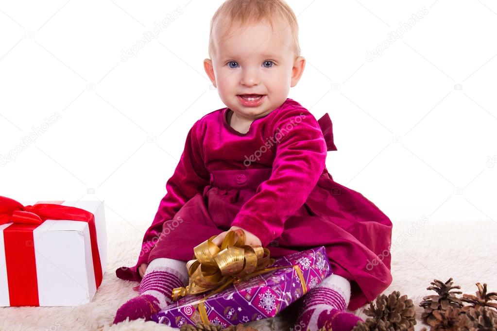 Beautiful baby girl in red dress in New Year's Eve smiling and holding a gift